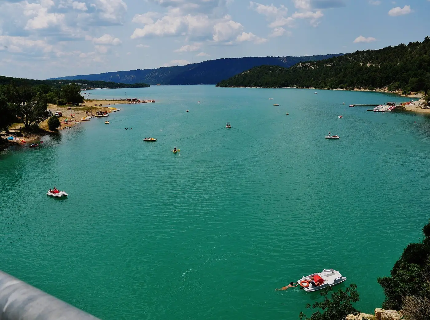 Pedal boats and swimmers on the turquoise waters of Lake Sainte-Croix, between two wooded shores